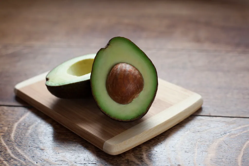 Un avocado tăiat în jumătate, pe un tocător
